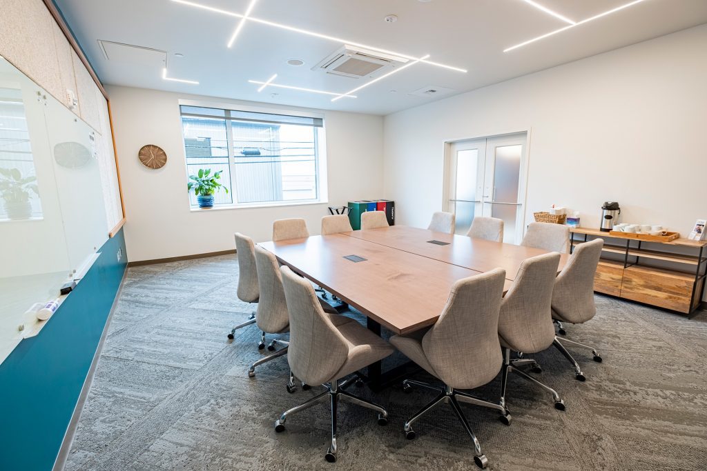 Photo of the interior of a small, well-lit meeting room with a large table and chairs around it.