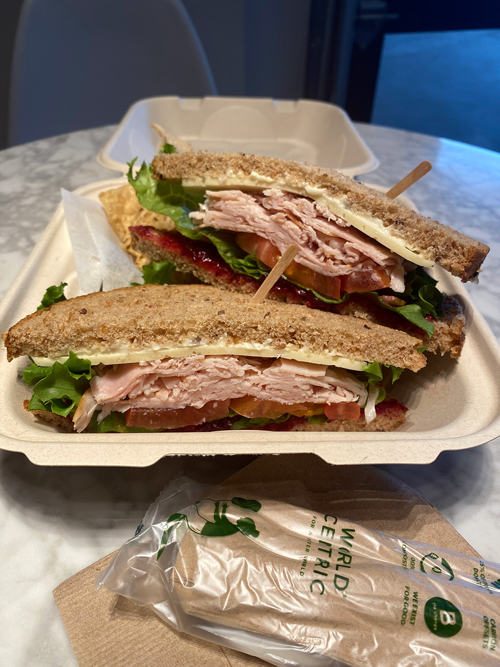 Photo of a turkey berry sandwich in a to-go container, with biodegradable cutlery.