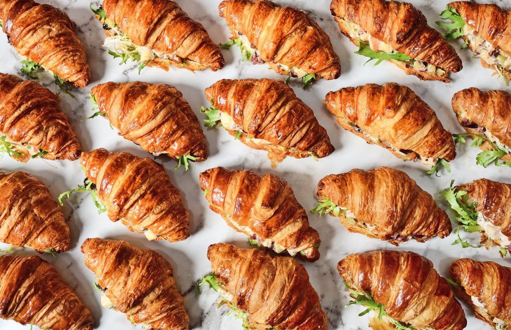 Overhead shot of croissant sandwiches, filled with greens and meats.