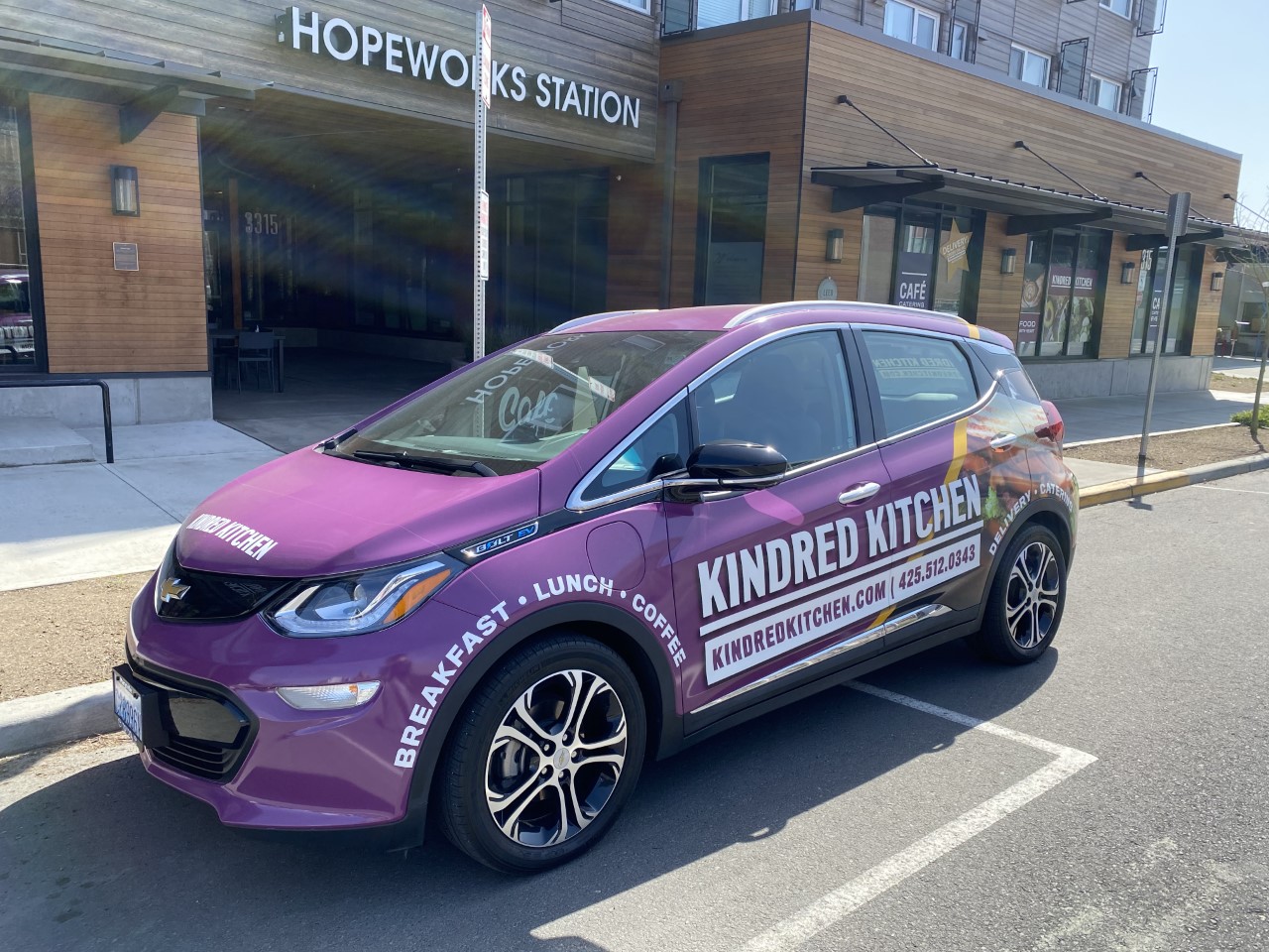 Photo of a purple Chevy Bolt EV with Kindred Kitchen vinyls, parked outside on the street.